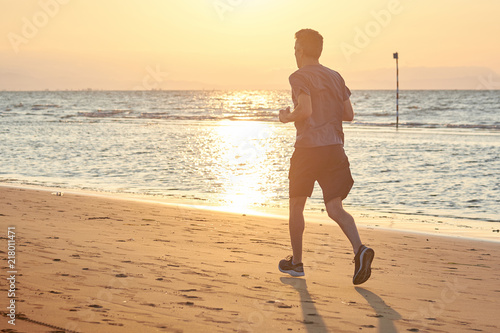 Uomo che corre sulla spiaggia all'alba photo