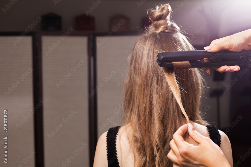 Fototapeta premium professional hairdresser curling a hair strand of a model with a topknot in a beauty salon. concept of stylist training