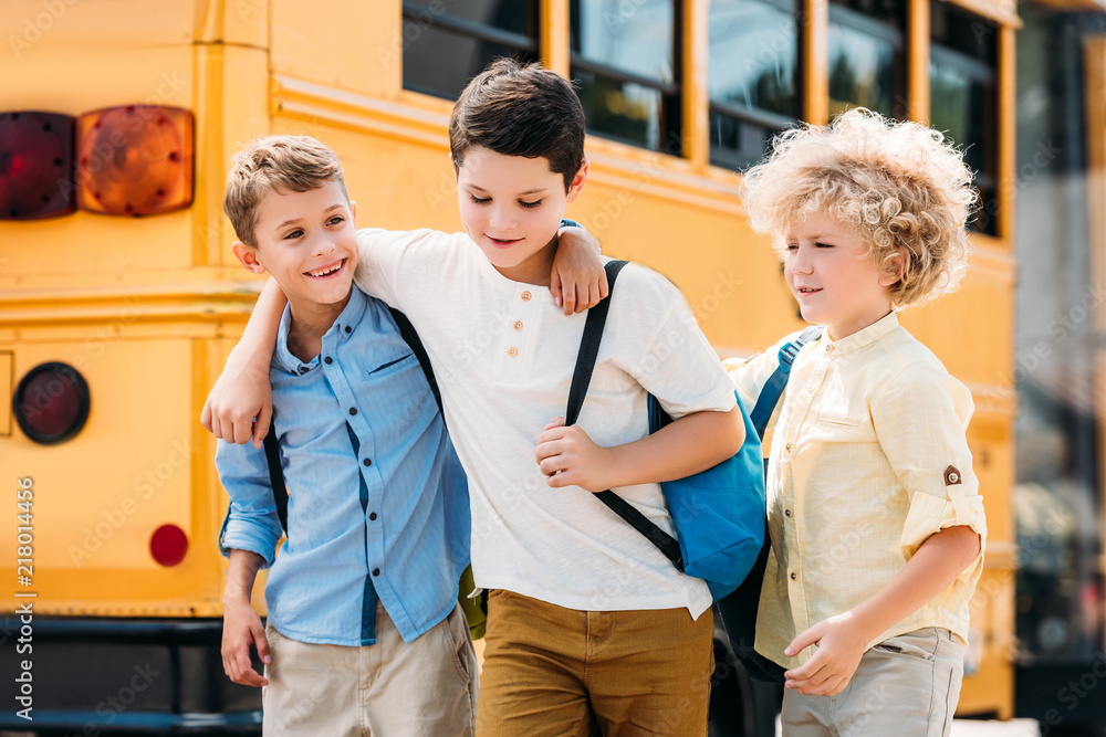 Fototapeta premium happy little schoolboys having fun together in front of school bus