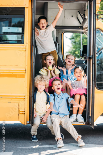 group of adorable schoolchildren sitting on stairs of school bus and screaming
