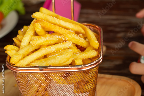 Fried potatoes in a sieve placed on a wooden tray.