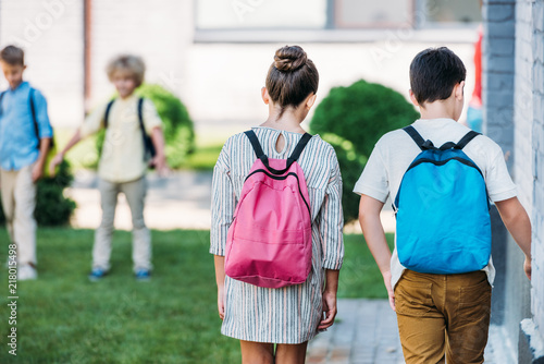 rear view of schoolchildren with bakpacks waling by school garden