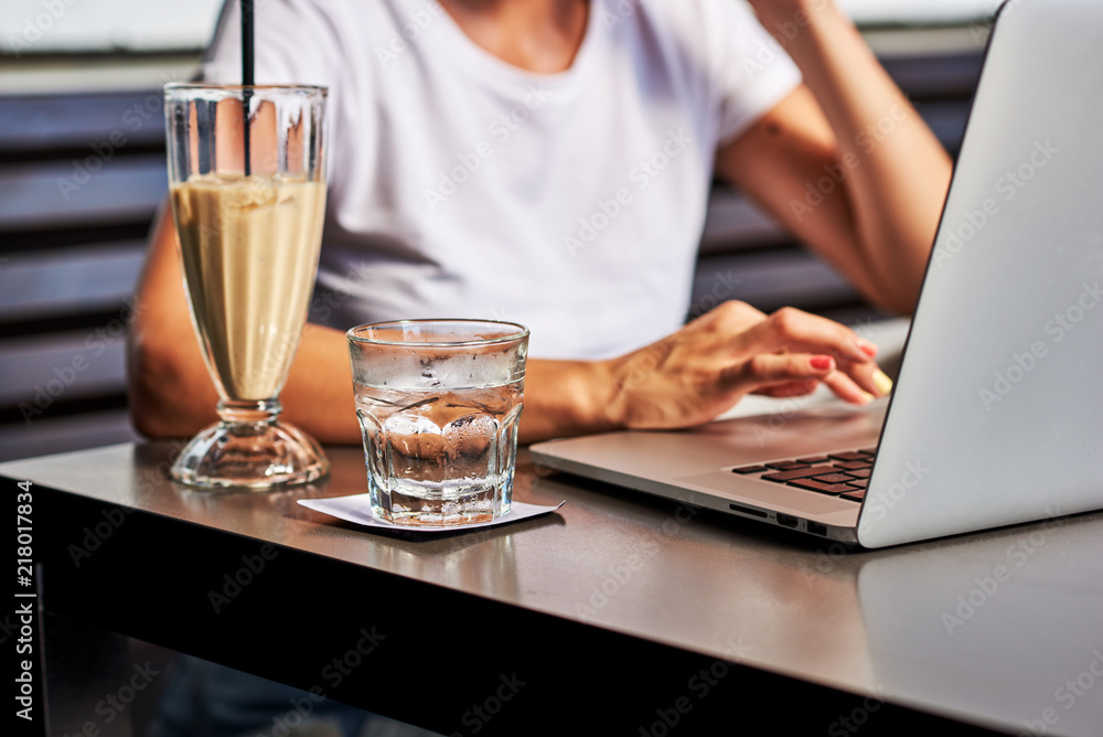Blurred of girl working at the notebook in a coffee shop. Selective focus on glass of water. Blurred of girl working at the notebook in a coffee shop. Selective focus on glass of water.