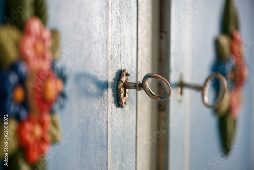 Decorative, vintage look ancient metal key in a blue, rustic doors in wardrobe keyhole. Beautiful flower ornaments. Concept of safety and secrets