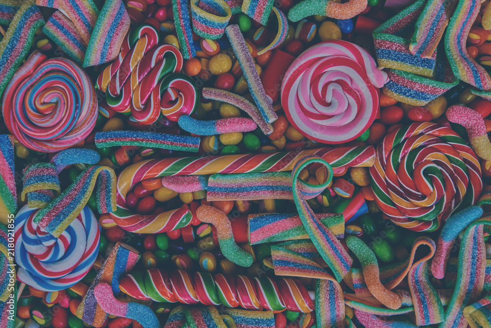 Colorful bright assorted  candy canes and rainbow colored spiral lollipops  with scattered marmalade, jellybeans and different colored round candy. Top view. Candy background.