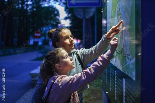 Two girls teenager are looking for the way route on the map scheme at night dark
