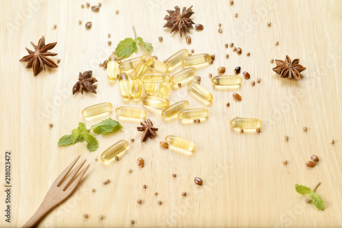 Fototapeta Naklejka Na Ścianę i Meble -  Medicine herb, Cod liver oil omega 3 gel capsules with healthy medicinal plant on wooden brown tone background with a wooden fork on foreground.