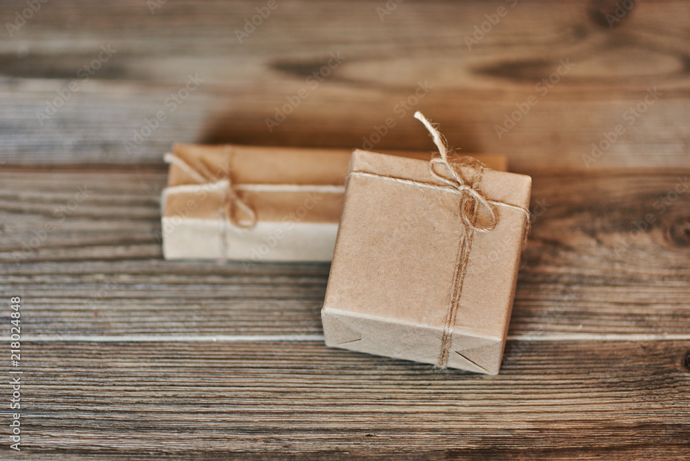 Boxes in craft paper, eco paper on the wooden table. Parcels or gifts tied with twine. Brown paper wrapped gift box with rope bow on a old rustic wood background. Background for your design. Boxes in craft paper, eco paper on the wooden table. Parcels or gifts tied with twine. Brown paper wrapped gift box with rope bow on a old rustic wood background. Background for your design.