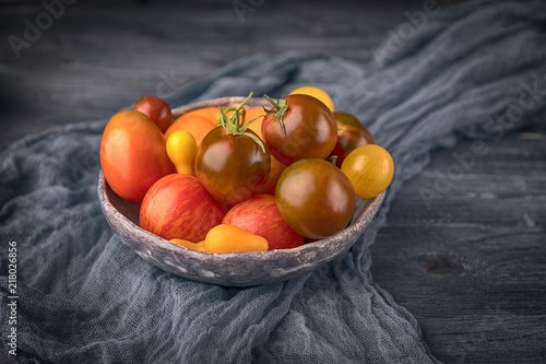 Ceramic bowl with various colorful tomatoes on wooden background. Free space