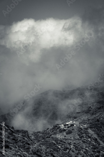 Schwarz-weiß-Aufnahme eines Hofes im Gebirge, verhangen in dichten Wolken