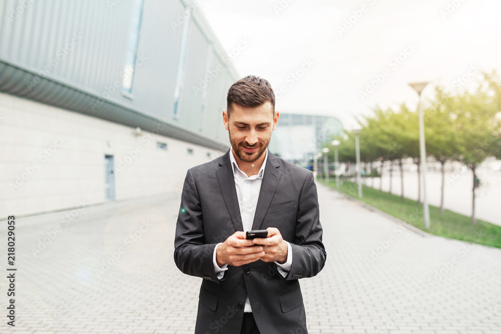 A handsome businessman using a smartphone. working by using smart phone in remote working concept. Business and information technology concept. standing street with city in the background A handsome businessman using a smartphone. working by using smart phone in remote working concept. Business and information technology concept. standing street with city in the background