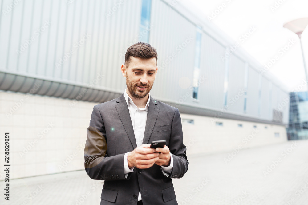 A handsome businessman using a smartphone. working by using smart phone in remote working concept. Business and information technology concept. standing street with city in the background A handsome businessman using a smartphone. working by using smart phone in remote working concept. Business and information technology concept. standing street with city in the background