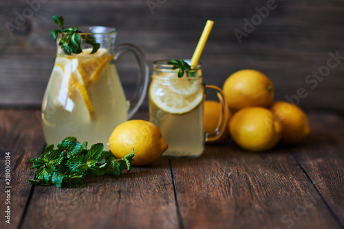 Homemade lemonade with mint and ice in jug, with fresh lemons over wooden background. Delicious and juicy lemonade, full of useful vitamins and antioxidants. Healthy and detox summer drink.