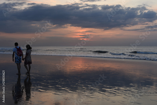 Silhouette romantic couple in love walking on the beach on bright sunset background. Happy young couple enjoying ocean sunset during travel. People on summer beach holiday. Vacation concept.