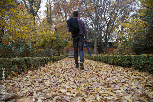 Young man walking by fallen leaves on the ground in a park a cloudy day © pablobenii
