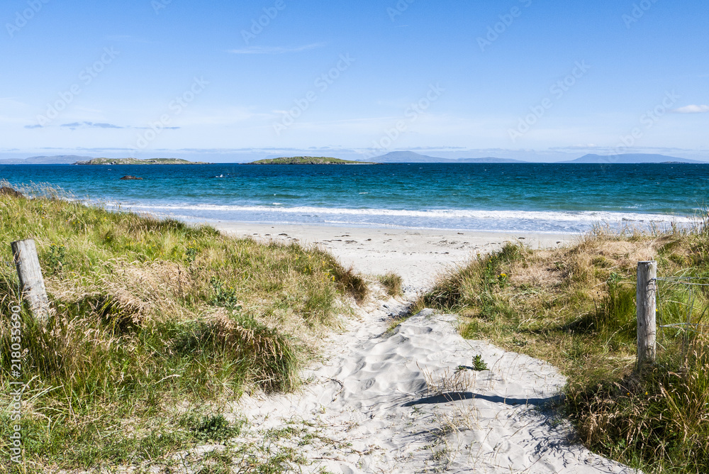 Sandy path to the beach on a sunny day with blue sky and mountains in the distance. Taken in Renvylle along the Wild Atlantic Way in Ireland in summer.