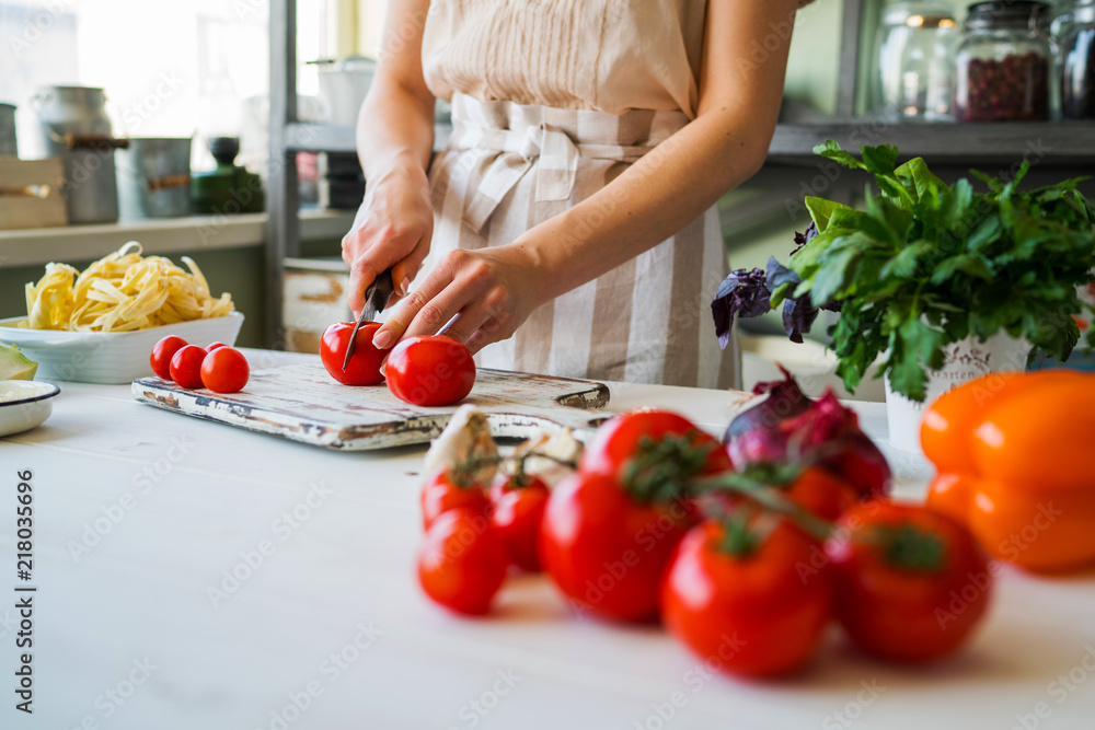 Close up of unrecognizable cook,cutting tomatoes and other vegetables with knife while working in home kitchen. Woman cooking salad, bio food preparing. Vegetarian food, health lifestyle concept.
