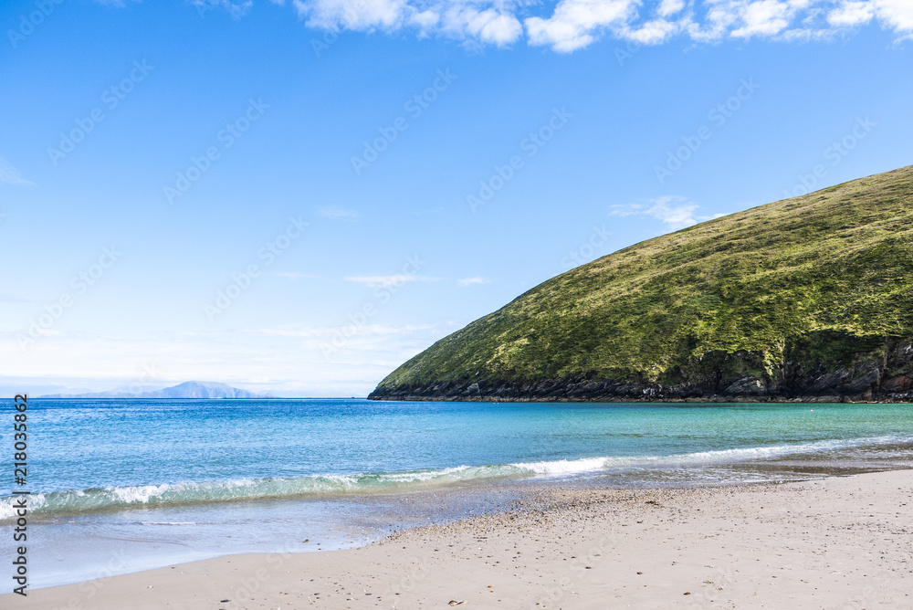 View of the beautiful Keem Bay on Achill Island in Ireland. Sandy beach, calm ocean, tall cliffs and blue skies. Taken in summer.