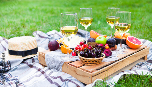 Picnic background with white wine and summer fruits on green grass, summertime party