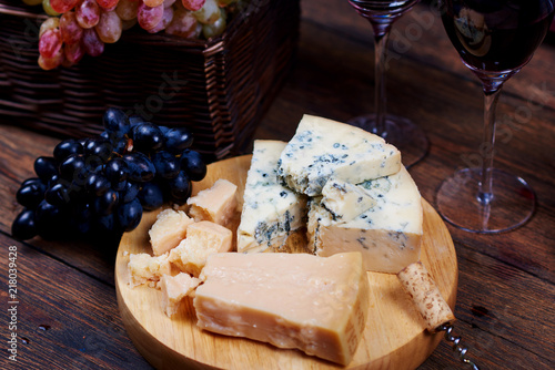 Closeup image of Danish Blue Cheese and Parmesan on platter near to basket with light bunch of grape for delicious wine degustation in rustic style.