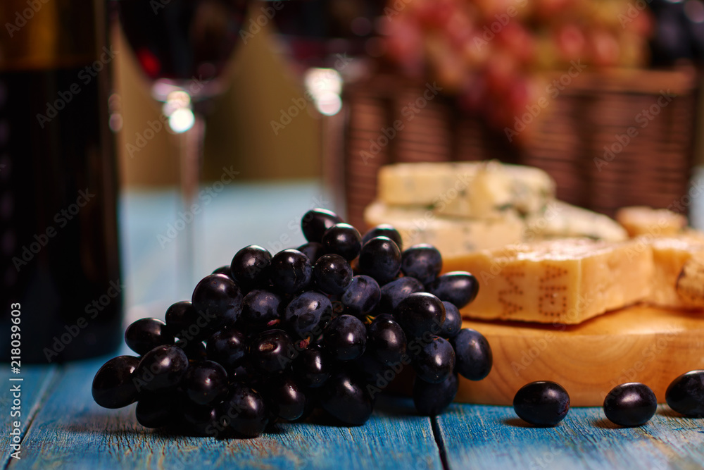 Obraz premium Closeup image of dark blue grape bunch lying on vintage table near to board with tasteful Roquefort slices for delicious degustation.