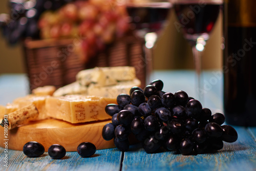 Organic fresh fruit and moldy cheese lying on retro table with basket on background.Delicateness healthy food and clusters of grape in rustic style.