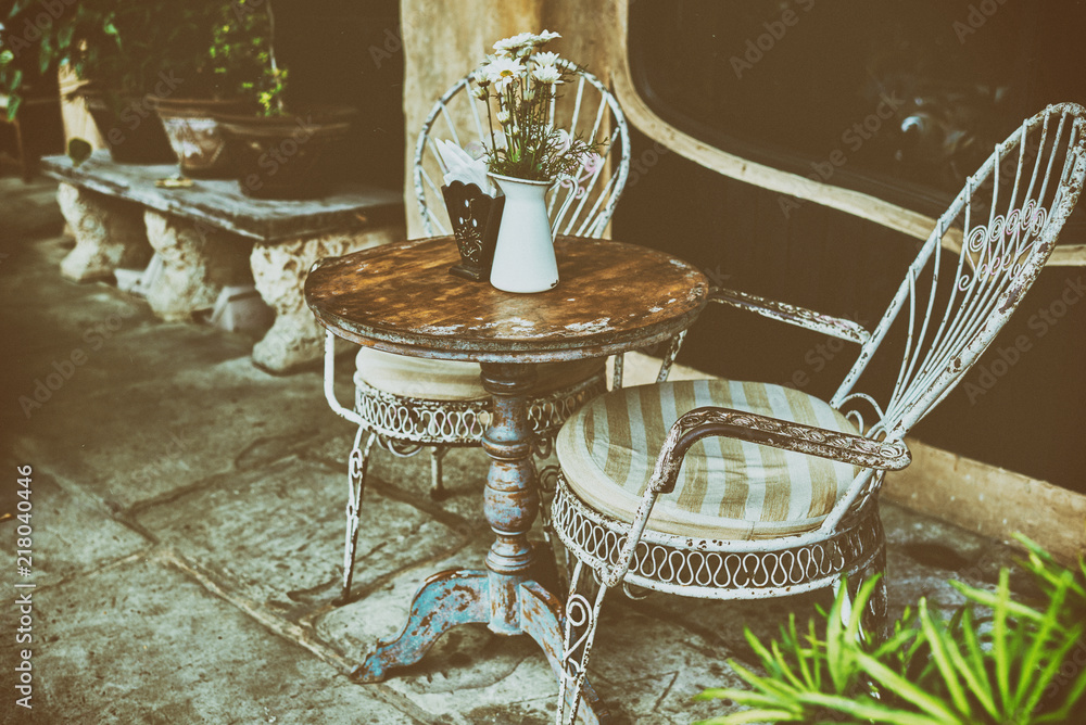 Old white antique wrought iron furniture, shabby chic exterior. Set of round table with flowers and two elegant chairs in the street in the old town. Table on cafe background. Vintage style.  .