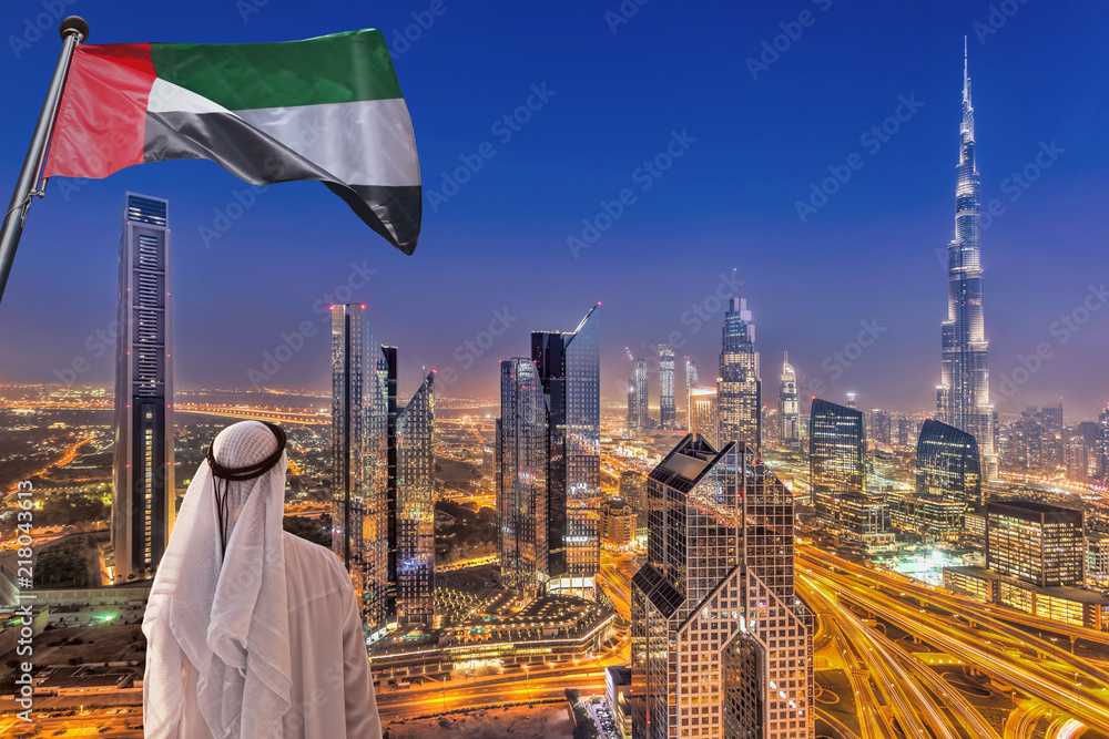 Naklejka premium Arabski mężczyzna ogląda nocny panoramę Dubaju z nowoczesną futurystyczną architekturą w Zjednoczonych Emiratach Arabskich