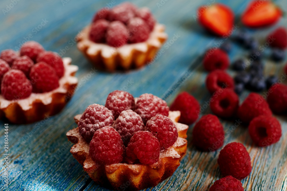 Delicious mini tarts made of oatmeal with fresh raspberries and custard on a wooden blue table. A homemade dessert made from delicious mini cakes. Healthy snack. Useful breakfast. Selective focus. Delicious mini tarts made of oatmeal with fresh raspberries and custard on a wooden blue table. A homemade dessert made from delicious mini cakes. Healthy snack. Useful breakfast. Selective focus.