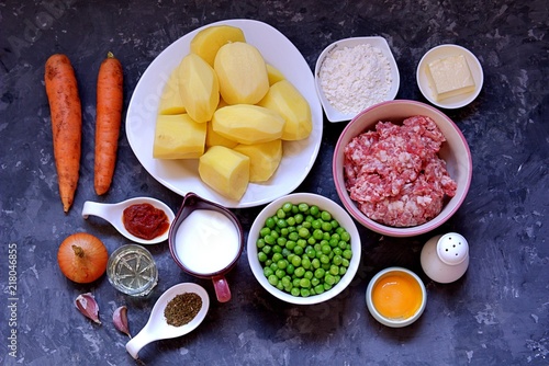 Ingredients for a "shepherd's pie", the British potato casserole with minced meat and vegetables. Peeled potatoes, minced meat, butter, milk, flour, egg yolk, carrots, green peas, onion, garlic, salt
