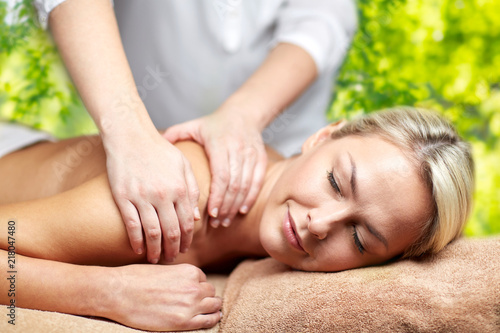beauty, wellness and relaxation concept - beautiful young woman lying having back massage in spa over green natural background