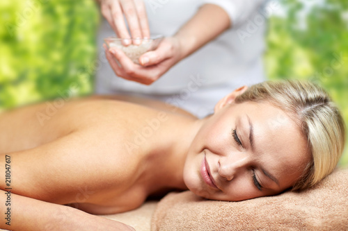 beauty, wellness and relaxation concept - close up of beautiful young woman lying with closed eyes and therapist holding salt bowl in spa over green natural background