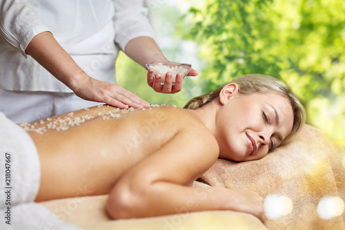 beauty, wellness and relaxation concept - beautiful young woman lying having salt massage in spa over green natural background