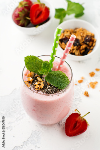 Pink strawberries, banana smoothie with granola and chia seeds in glass on light white concrete background. Top view. Copy space.