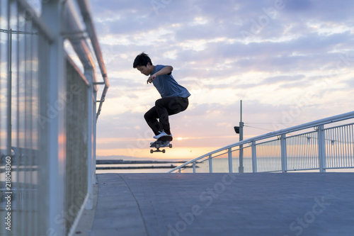 Young Chinese man skateboarding at sunrise near the beach