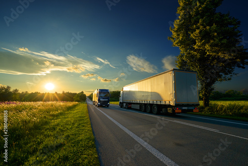 Trucks driving against each other on an asphalt road in a rural landscape at a golden sunset