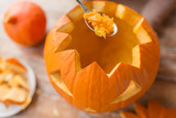 halloween, decoration and holidays concept - close up of spoon carving pumpkin flesh and making jack-o-lantern at home