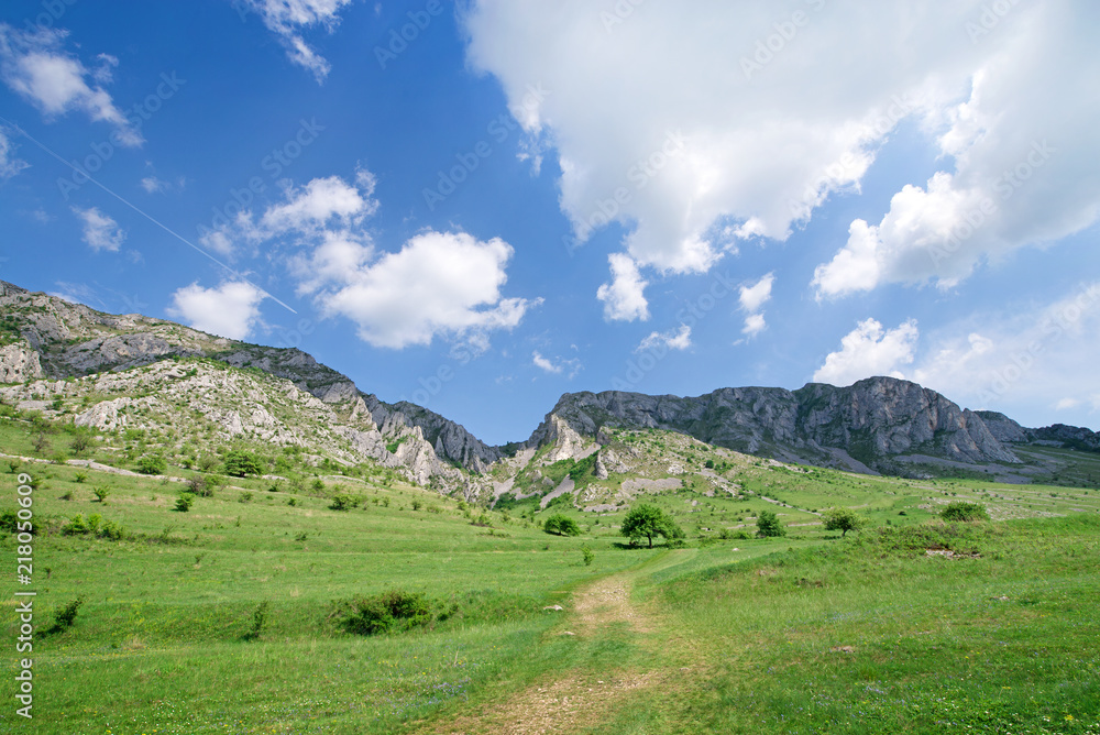 Sunny summer day, white clouds over mountain peak, where tourists climb to conquer fear, find courage and develop lateral thinking skills to overcome the difficulty of climbing a mountain. Small road