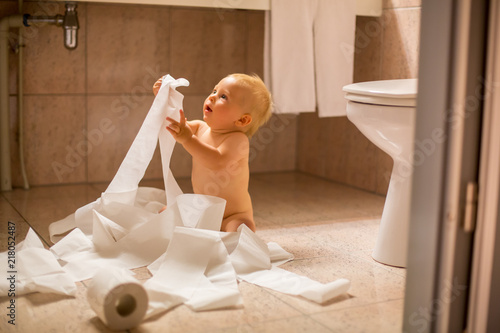 Toddler baby boy, ripping up with toilet paper in bathroom. photo