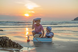 Sailor baby boy, cute child, playing on the beach with wooden boat, fishes and fishing rod on sunset