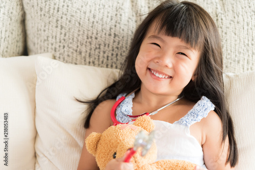 Cute little girl is smiling and playing doctor with stethoscope and teddy bear. Kid and health care concept.