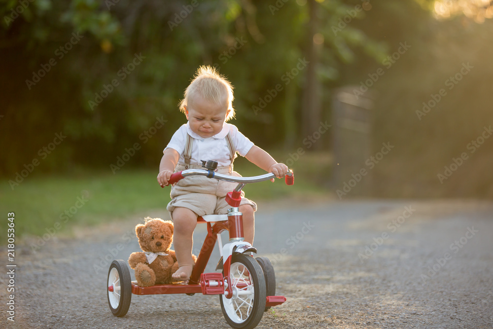 Cute toddler child, boy, playing with tricycle in backyard on sunset Cute toddler child, boy, playing with tricycle in backyard on sunset