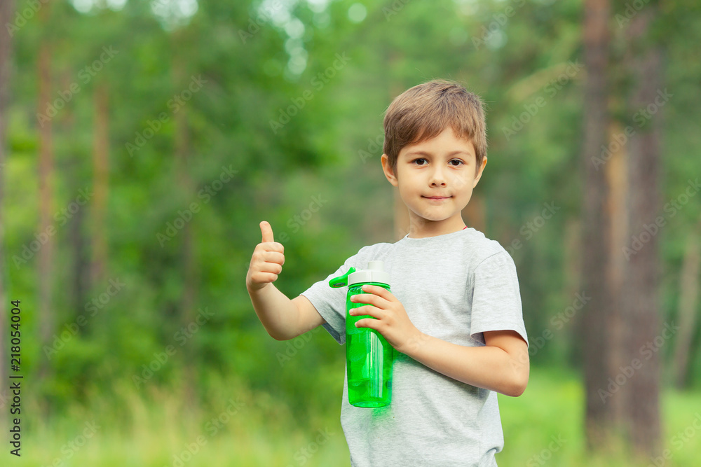 Little boy drinking water from bottle outdoors. Child approve a healthy diet and sport, showing thumbs up. Copy space. Little boy drinking water from bottle outdoors. Child approve a healthy diet and sport, showing thumbs up. Copy space.