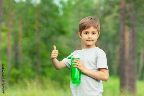 Little boy drinking water from bottle outdoors. Child approve a healthy diet and sport, showing thumbs up. Copy space.
