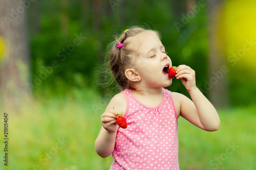 Little girl eating strawberry in nature. Child enjoys a delicious berry.
