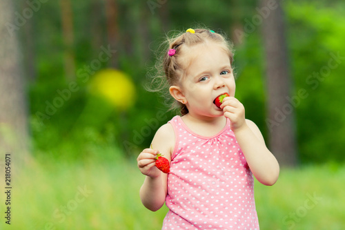 Little girl eating strawberry in nature. Child enjoys a delicious berry.