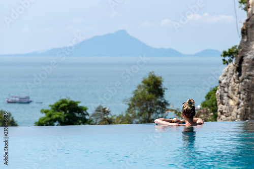 Woman relaxing in infinity swimming pool looking at view