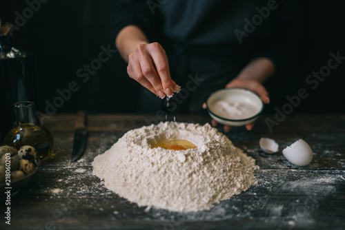 Homemade pasta is being processed. Woman kneads dough for pasta on wooden board. Rural kitchen interior and woman hands making fresh pasta dough. Food and cooking concept.