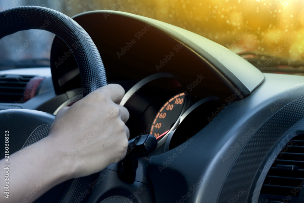 Man holding steering wheel of car control modern car view inside console on evening with orange of sunset and drop water of rain on the glass.