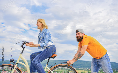Woman rides bicycle sky background. Push and promoting. Impulse to move. Man pushes girl ride bike. Support helps believe in yourself. Feel impulse to start moving. Girl cycling while man support her